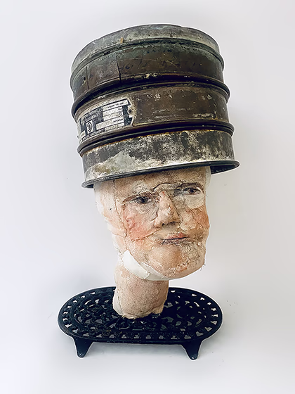 Head sculpture on a iron trivet with a head piece of three stacked laboratory sieves
